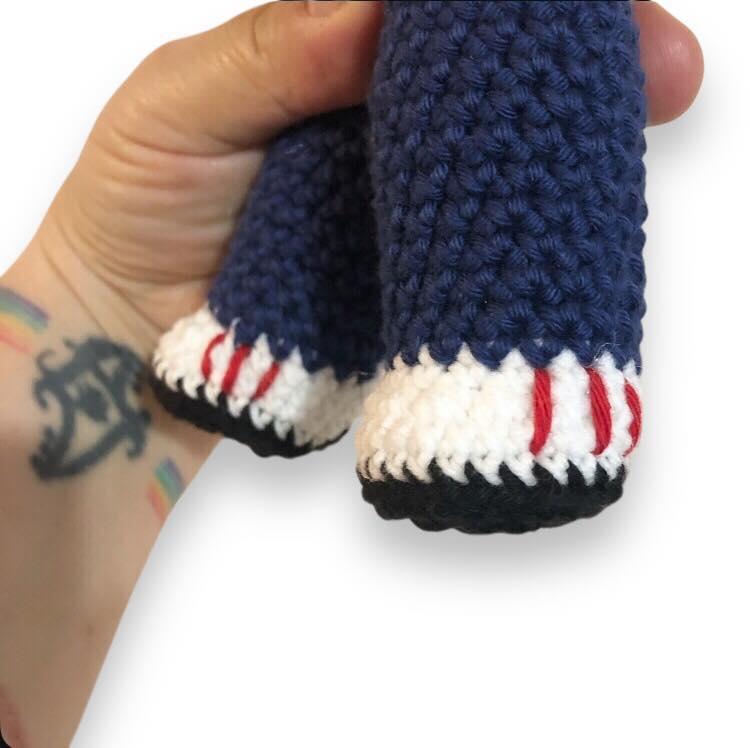 A close up of Arthur's crocheted leg pieces, blue pants and white shoes with red stripes and black bottoms.