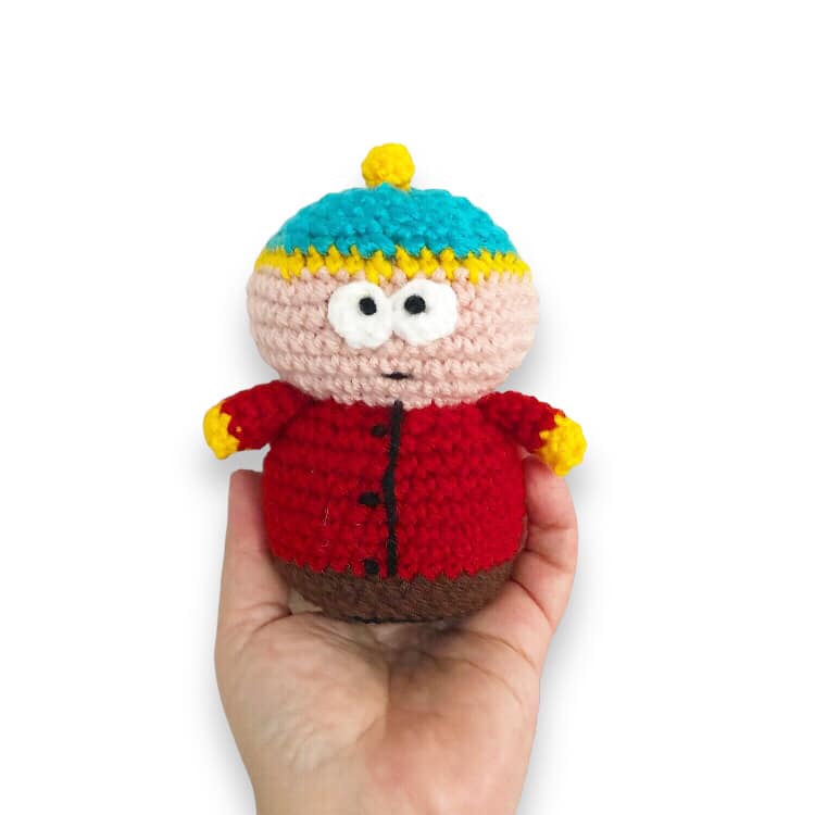 A crochet version of Cartman from South Park held up against a white background.