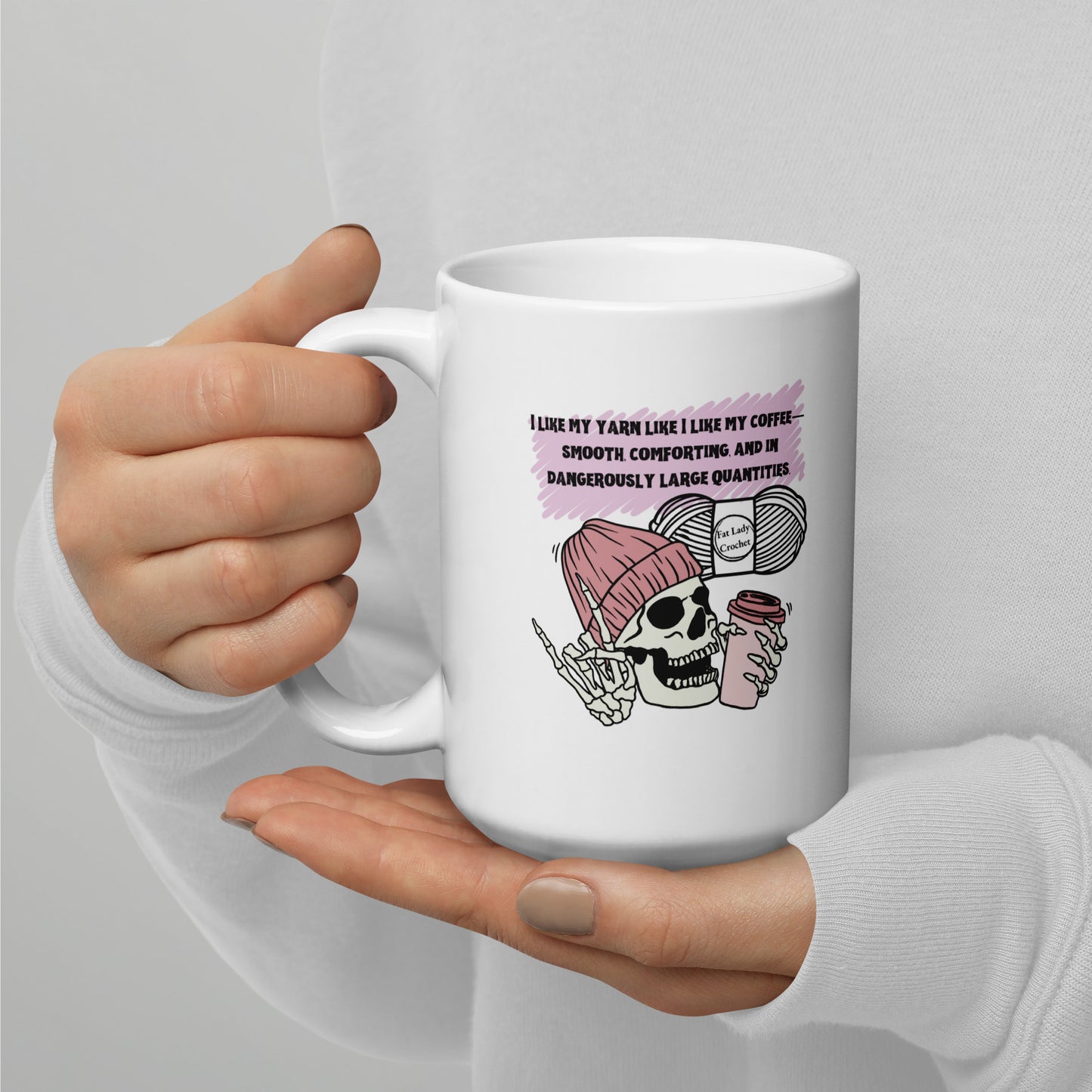 White mug with skull and coffee design held by a person against a gray background