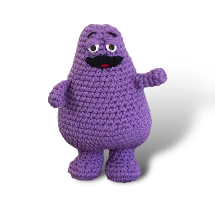 A crochet doll of Grimace standing against a white background.