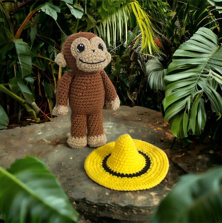 Crochet curious george in a jungle setting standing next to yellow hat