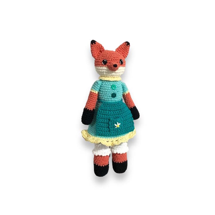 A crochet fox doll with a blue dress and bloomers standing against a white background.