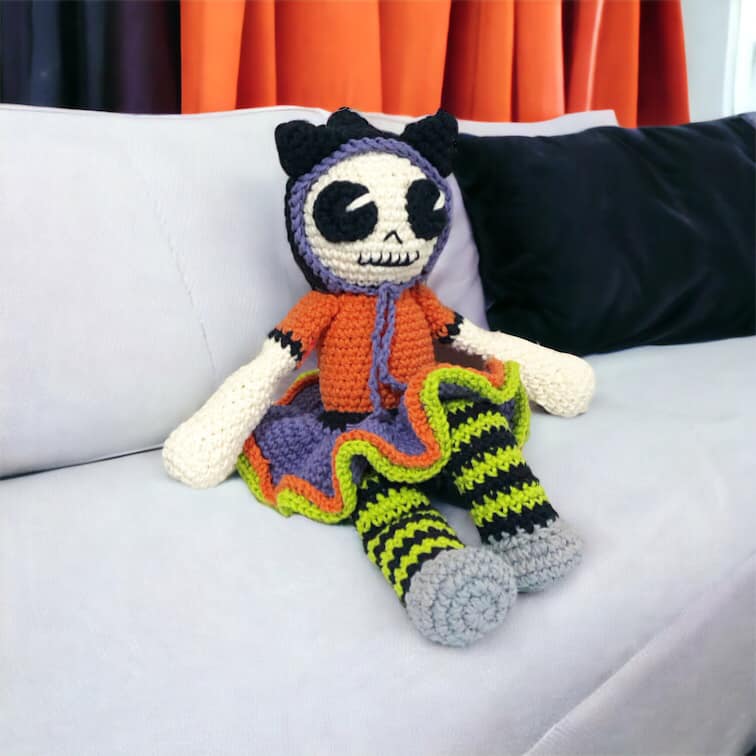 Crocheted skeleton doll with colorful outfit on a white couch