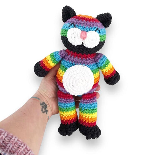 A crocheted rainbow cat doll being held up against a white background.