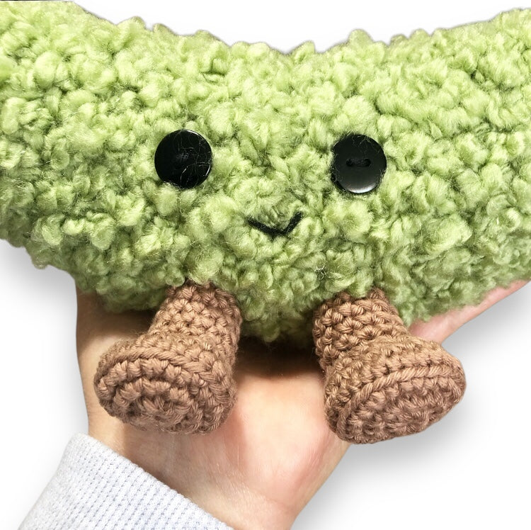 A close up of a crochet dill pickle being held against a white background.