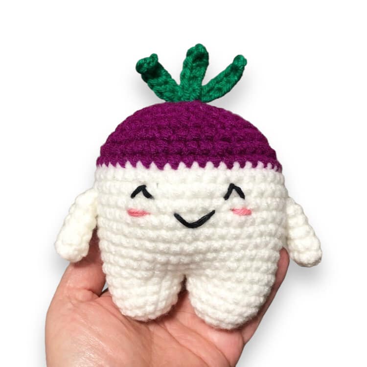 A crocheted doll of a cute turnip being held up against a white background.