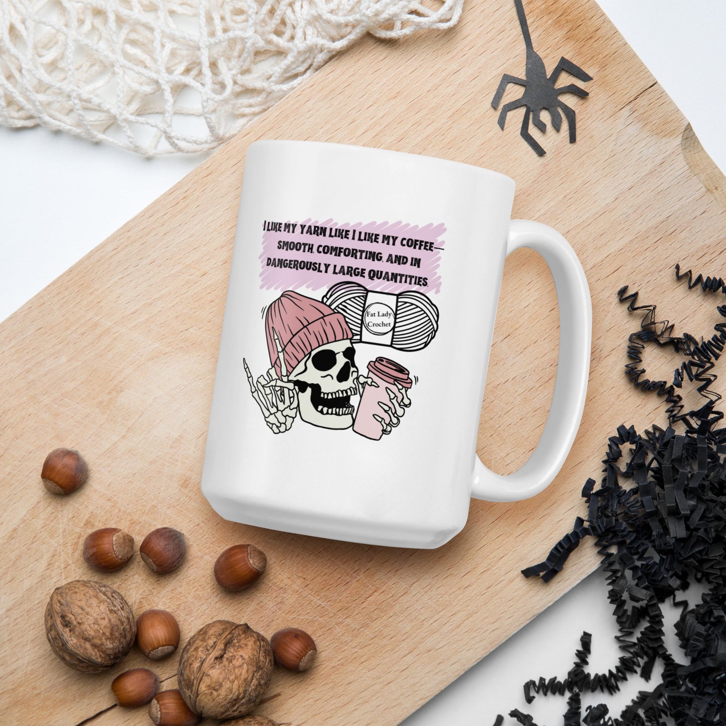 White mug with skeleton wearing a dark pink beanie holding a coffee mug with Halloween and autumn decorations surrounding it.