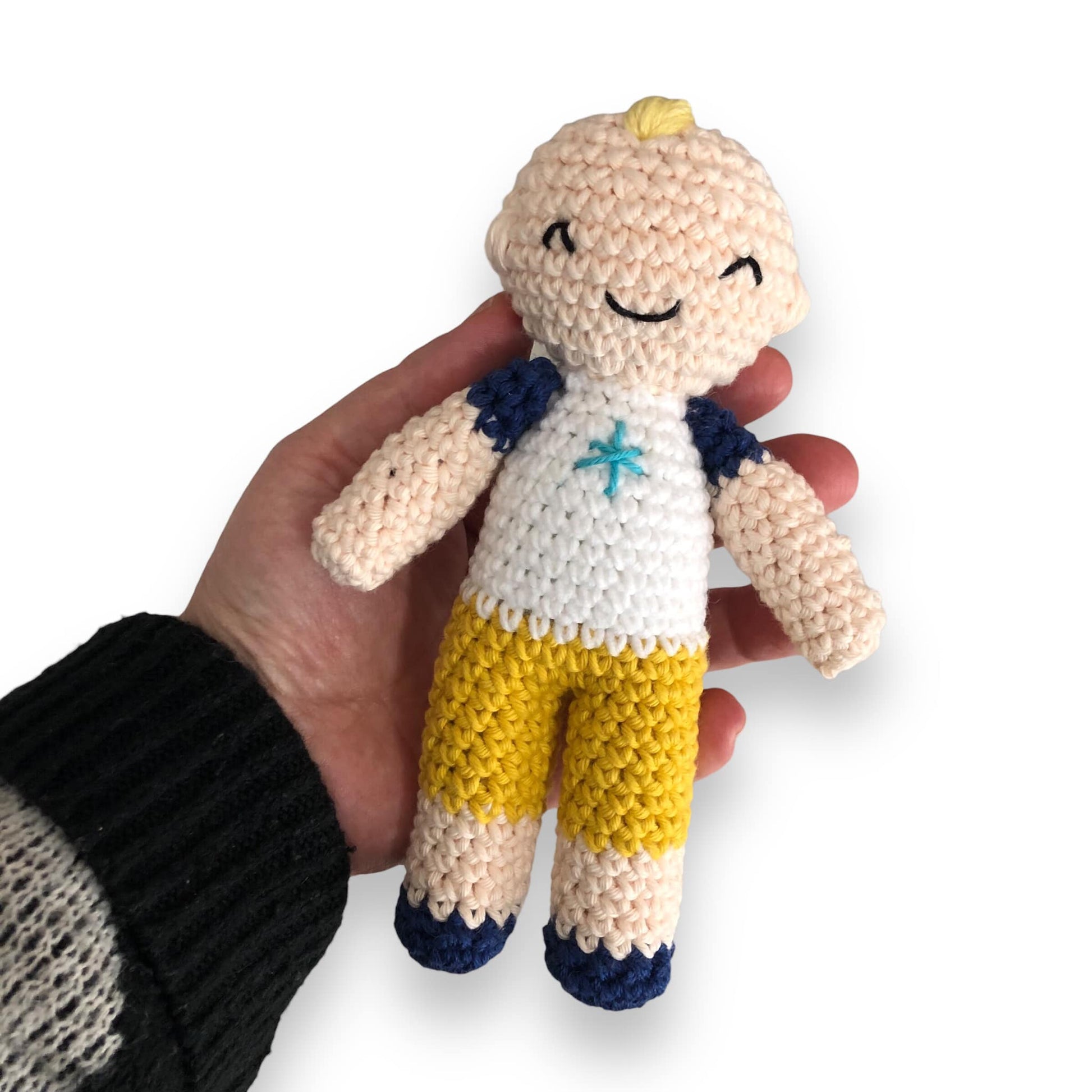 A crocheted JJ Doll being held up against a white backdrop.