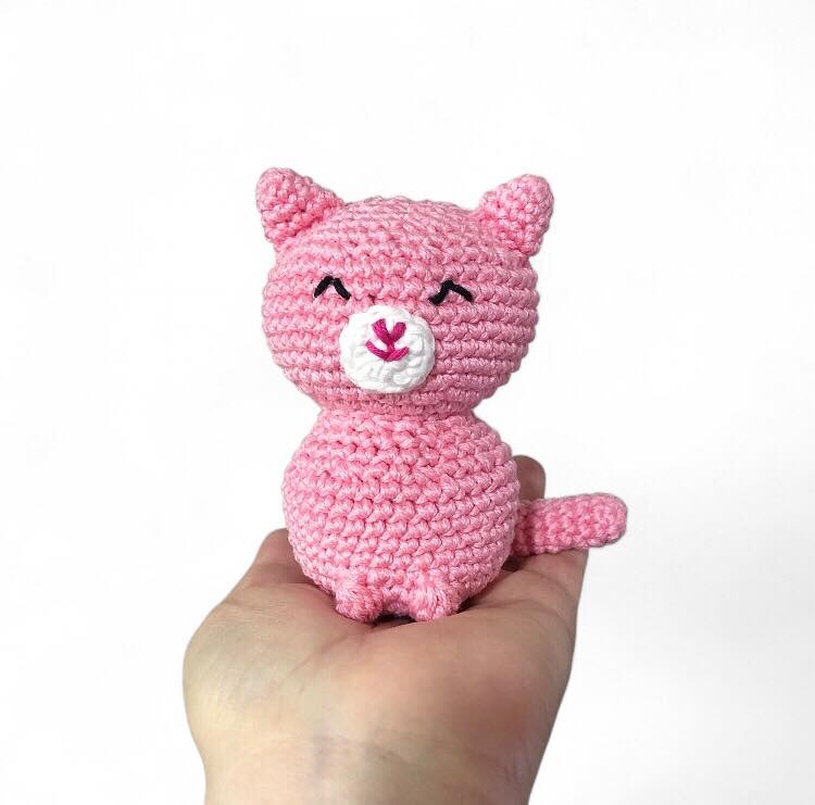 Pink crochet cat named custard held in a hand against a white background