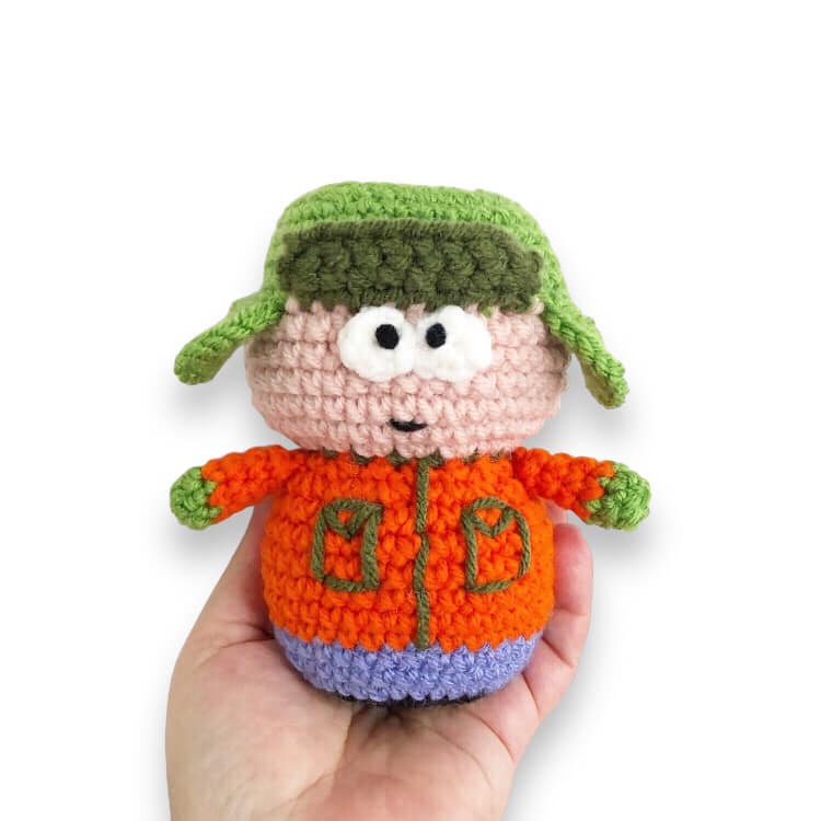 A crocheted version of Kyle from South Park being held up against a white background.
