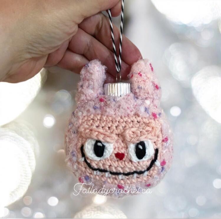 Labubu ornament being held by a hand against a white sparkly background.