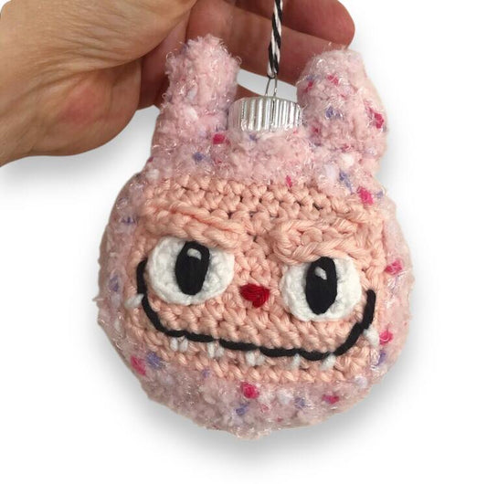 Pink Labubu ornament with a hand holding it against a white background