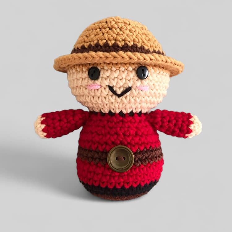 A crocheted doll resembling a Canadian Mountie standing against a white background.