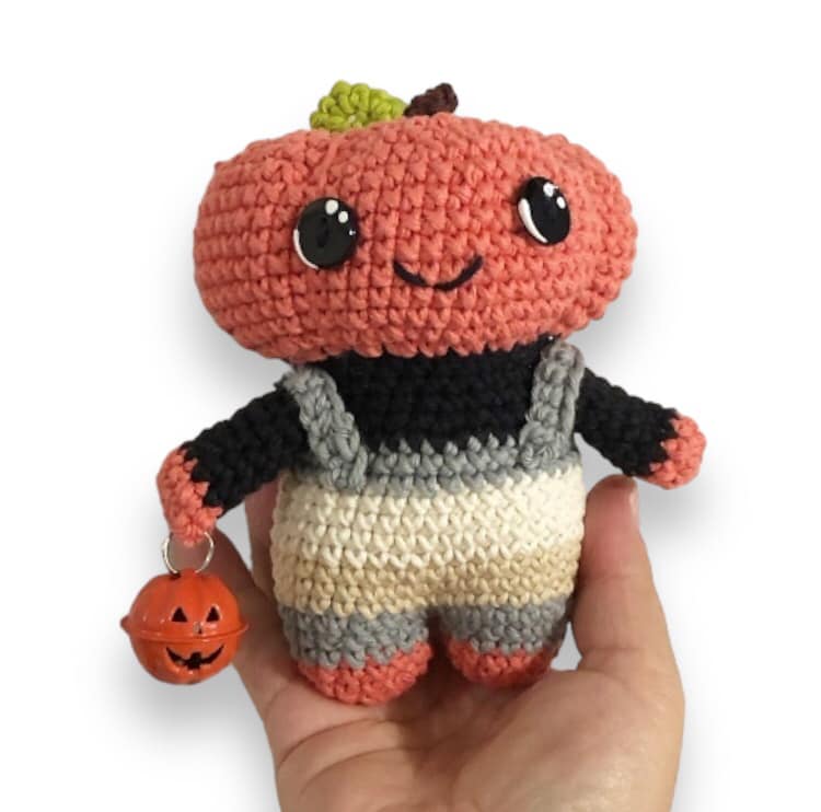 A little character with a pumpkin head and smiley face being held up against a white background.