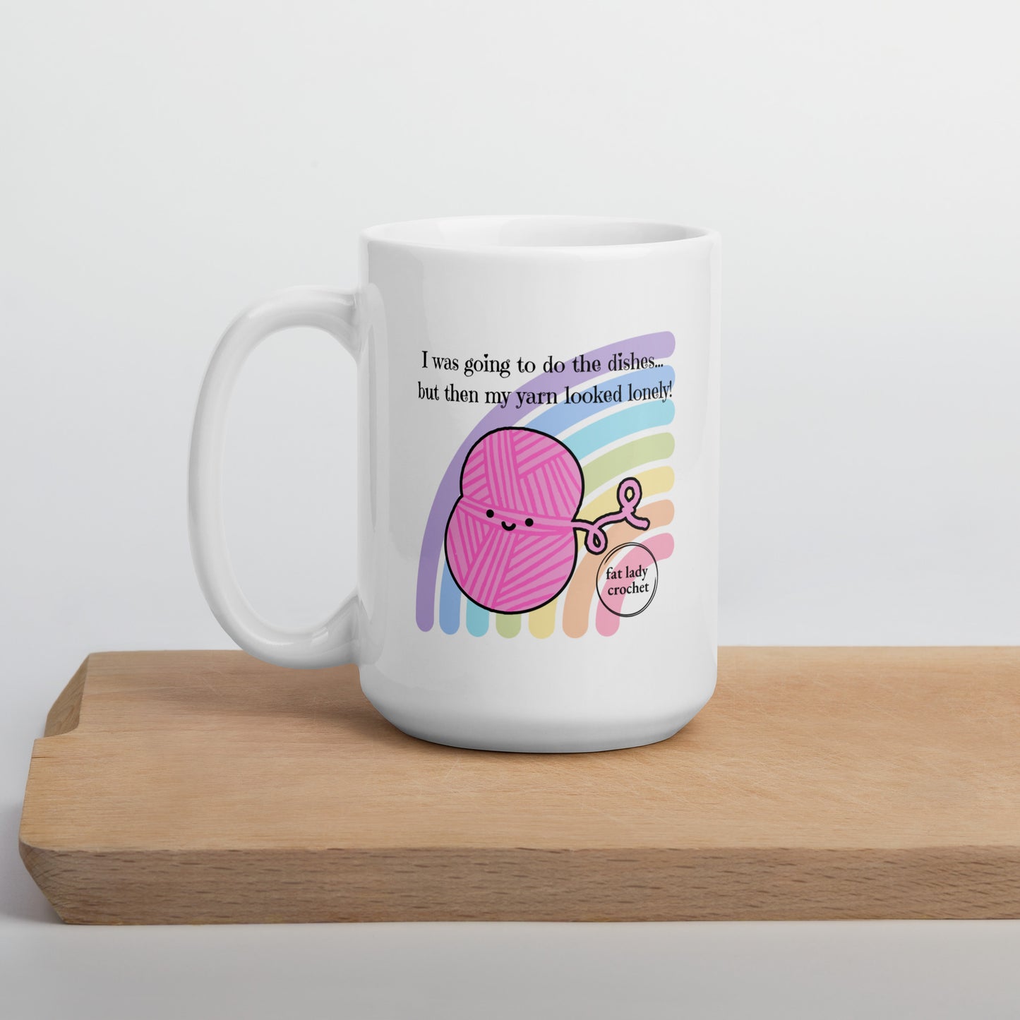 White porcelain mug with pink yarn that has a smiley face against a pastel rainbow.