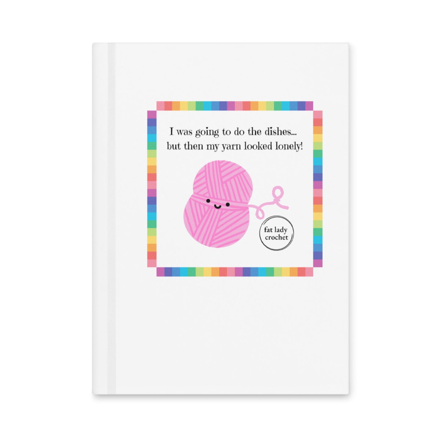 White journal with the quote "I was going to do the dishes...but my yard looked lonely!" on it with a pink smiling yarn ball set inside a rainbow border.