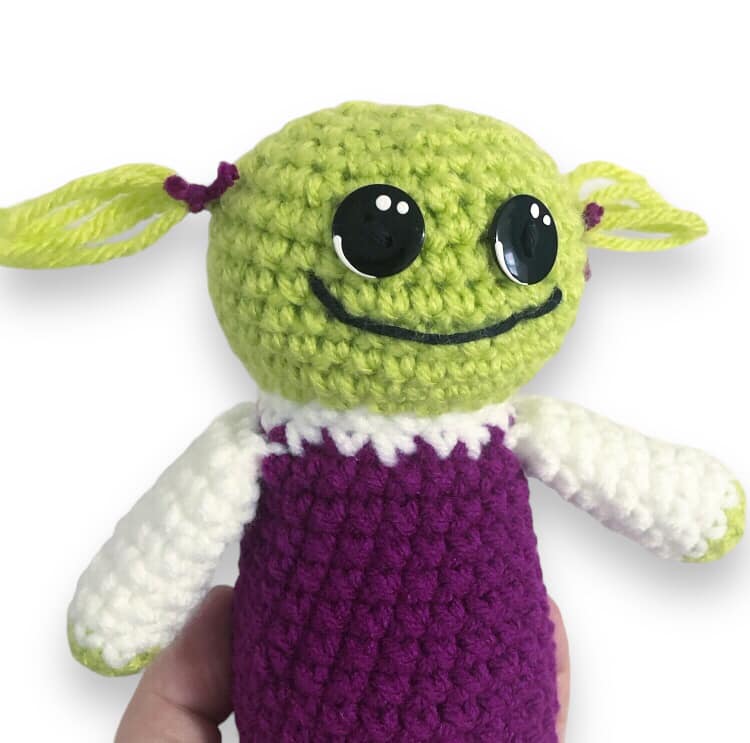 A crocheted doll of Mona from Nanalan being held up against a white background.