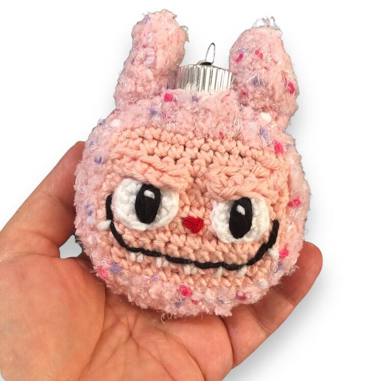 Pink Labubu ornament being held by a hand against a white background.