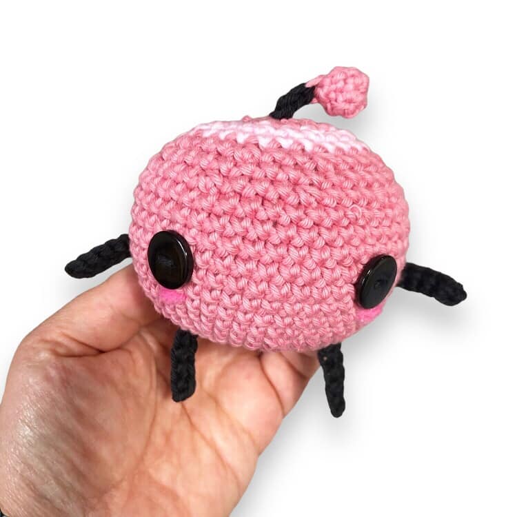 A pink crochet junimo being held up against a white background.