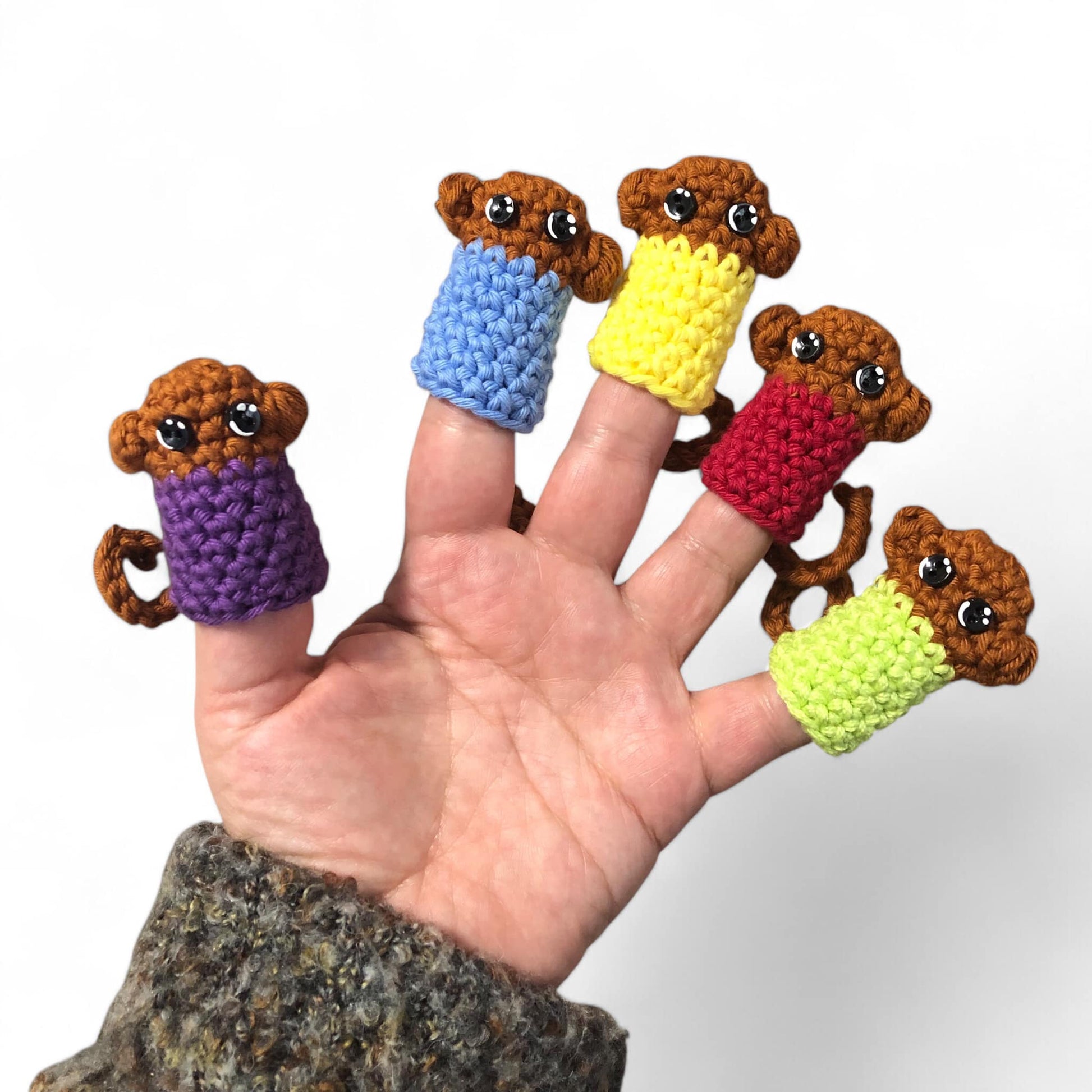 A hand displaying five little monkey finger puppets with different colored shirts in purple, yellow, blue, green, and red.