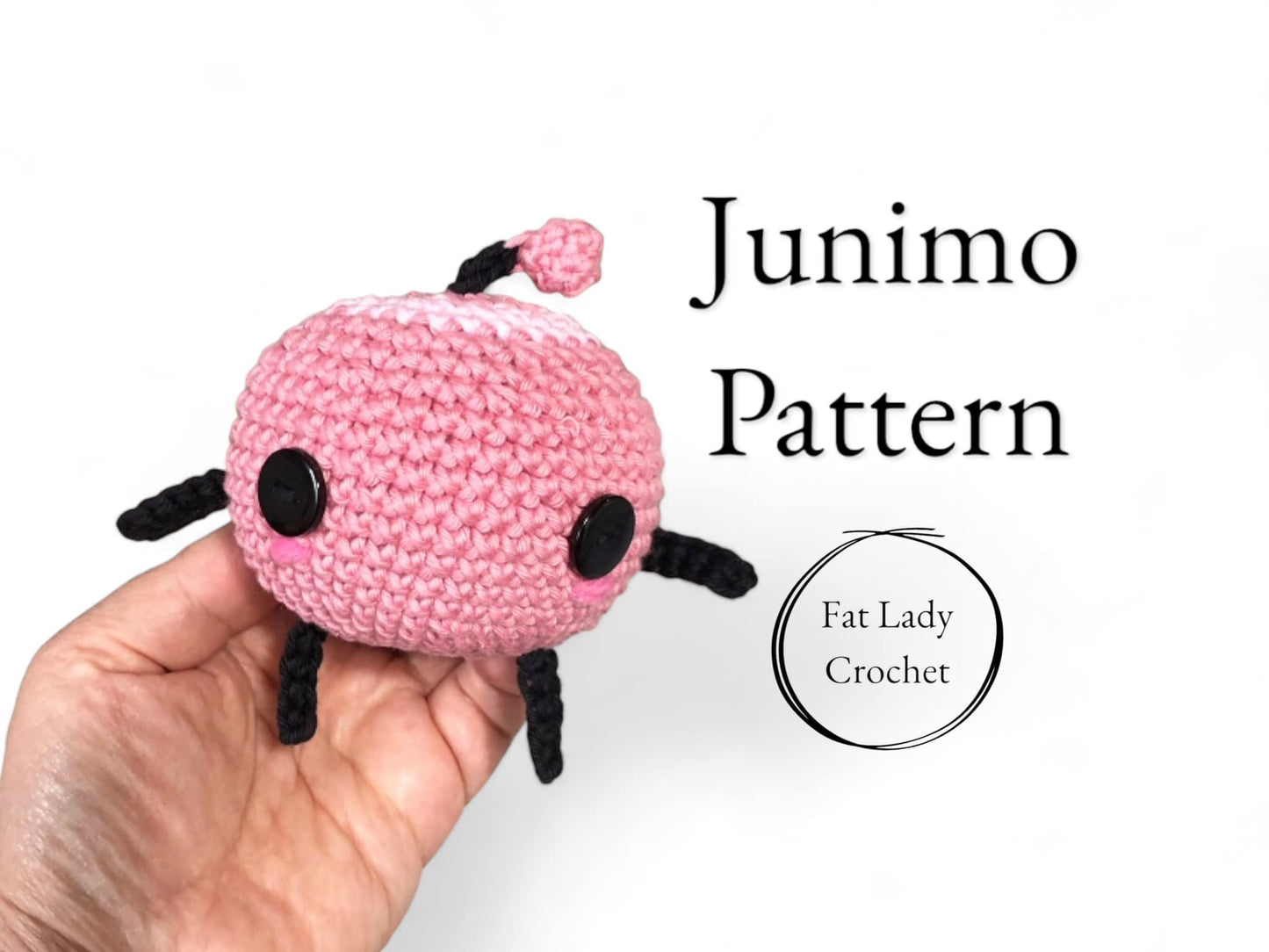 A crochet Junimo pattern being held in a person's hand, with a pink body, black limbs and a pink leaf, and the text 'Junimo Pattern' and 'Fat Lady Crochet' visible.