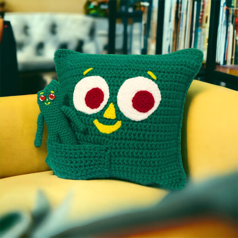A crochet Gumby doll and Gumby pillow on a yellow couch.