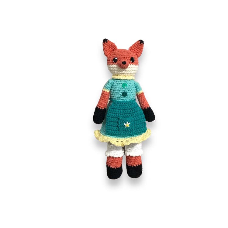 A crochet fox doll with a blue dress and bloomers standing against a white background.