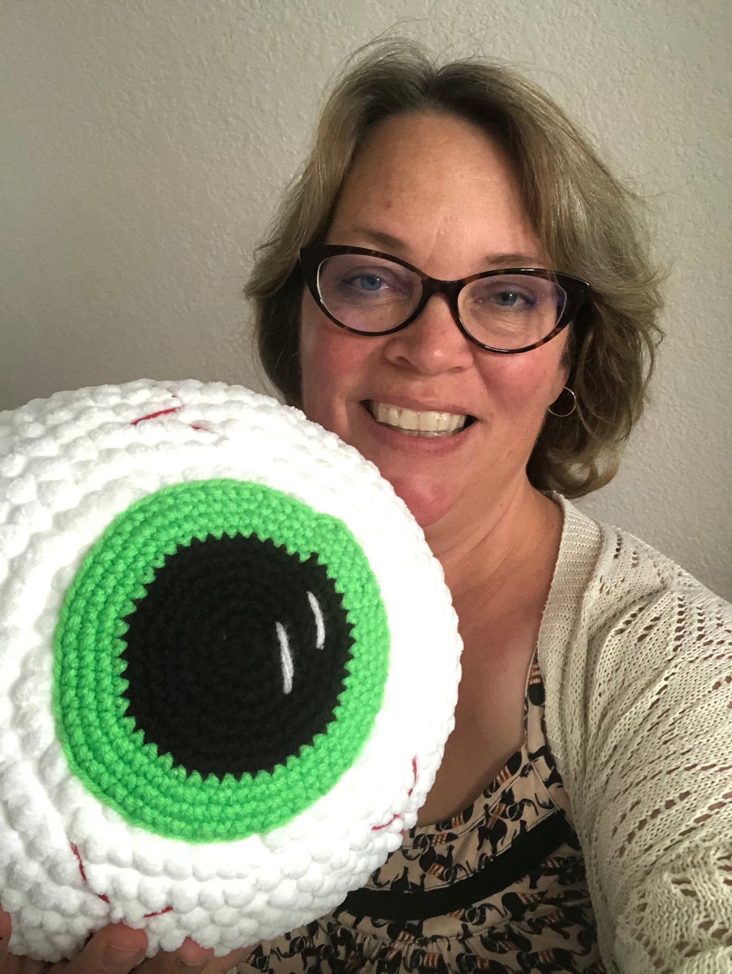 A woman holding up a giant crochet eyeball and smiling.