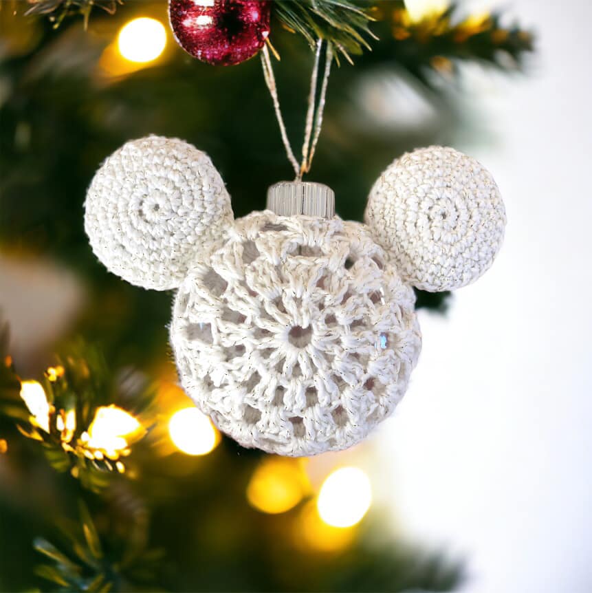 A crocheted white Mickey Mouse ornament hanging on a Christmas Tree.
