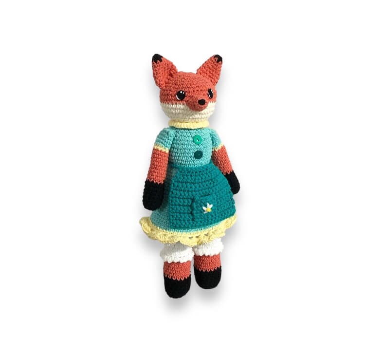 A crochet fox doll with a blue dress and bloomers standing against a white background.