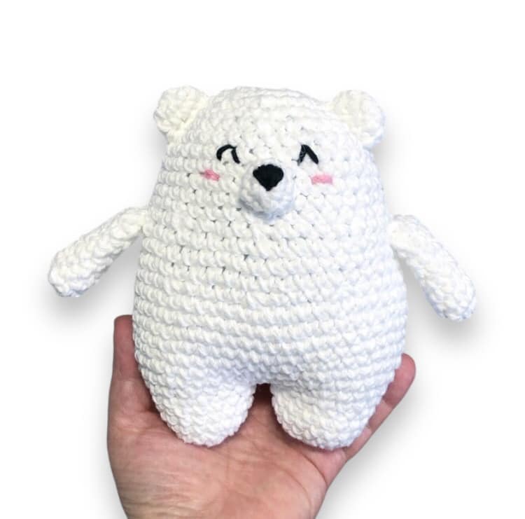 A crochet doll resembling a chubby bear being held up against a white background.