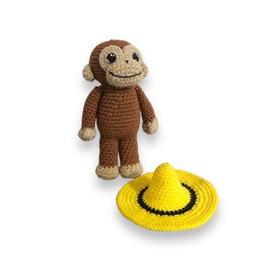 A crochet doll depicting a brown monkey (Curious George) and a yellow hat.