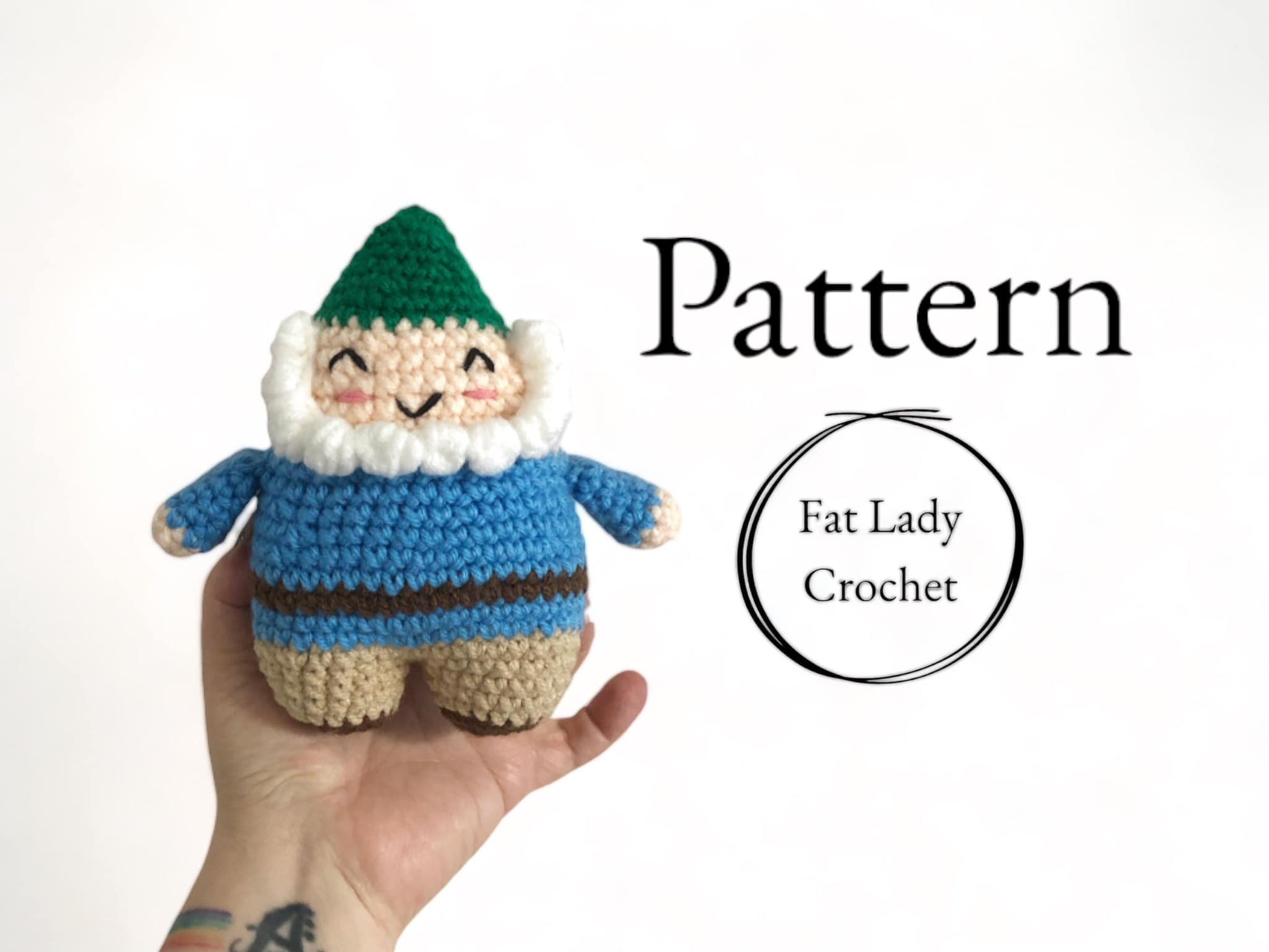 A crocheted doll of a smiling garden gnome with a green hat, blue jacket, beige pants, and a white beard being held up against a white background with text that reads "Pattern," and "Fat Lady Crochet."