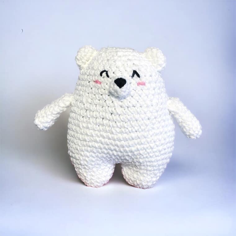 A crochet plushie resembling a polar bear standing against a white background.
