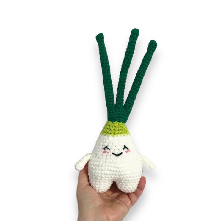 A crocheted doll resembling a green onion being held up against a white background.