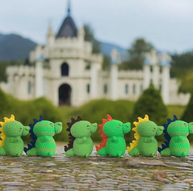 A group of small crochet baby dragons with different coloured spines against a background with a white castle.