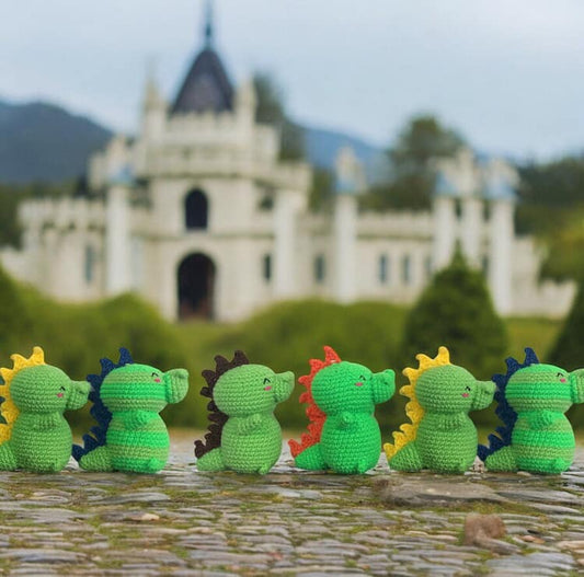 A group of small crochet baby dragons with different coloured spines against a background with a white castle.