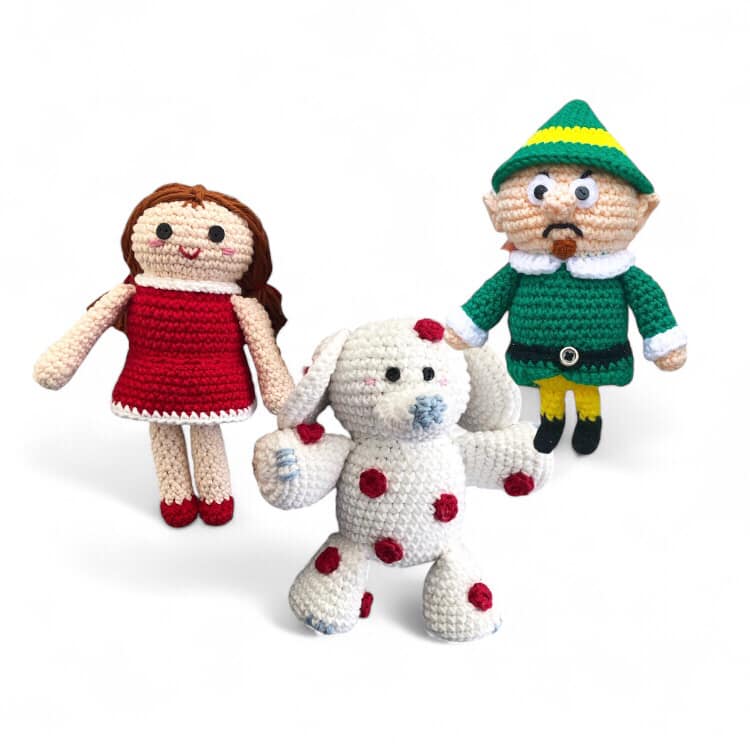 Three crochet dolls resembling some cast members from Rudolph the Red-Nosed Reindeer cast. A crocheted doll in a red dress, a white elephant with red spots, and a grumpy elf with a goatee and green outfit.