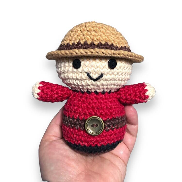 A crochet doll resembling a Canadian Mountie being held against a white background.
