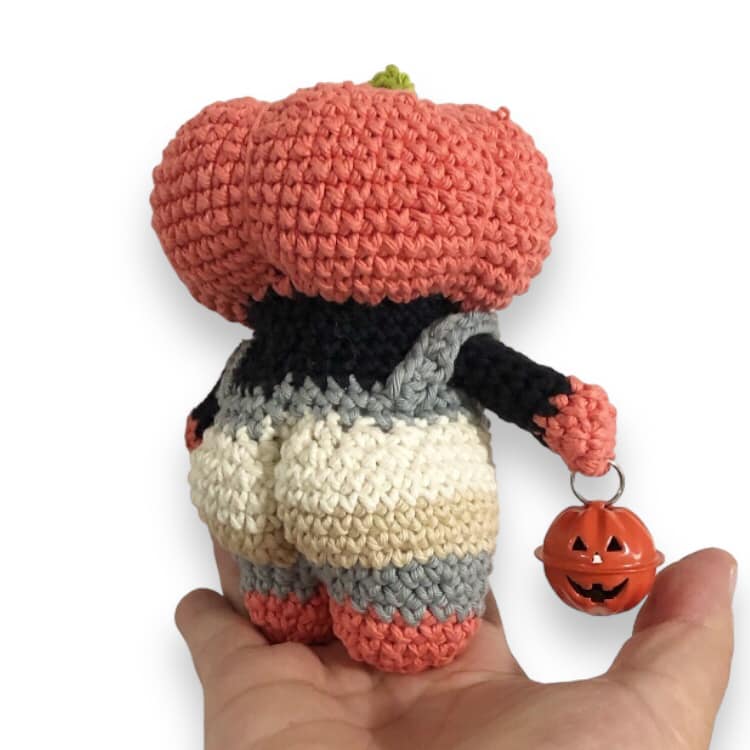 A behind view of the crochet pumpkin head doll with a bubble butt being held up against a white background.