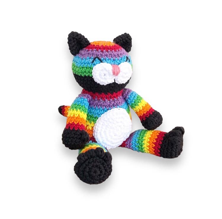 A crocheted doll resembling a rainbow cat sitting against a white background.