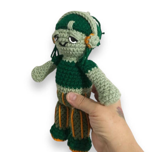 A crochet doll resembling Carmella Creeper being held up against a white background. 