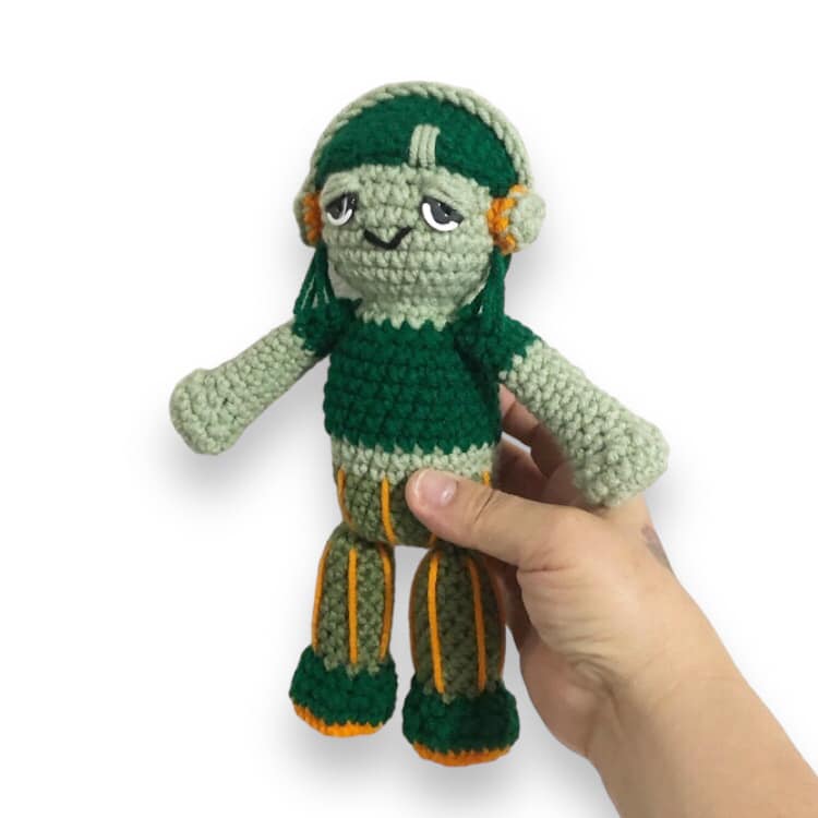A crochet doll resembling Carmella Creeper being held up against a white background. 
