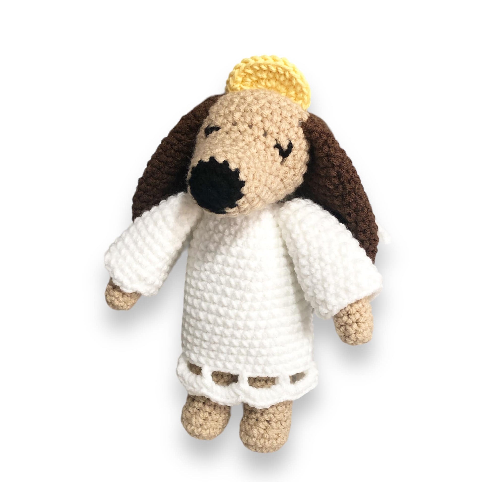 A crochet dog dressed as an angel standing against a white background. 