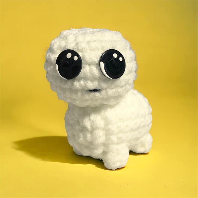 A crocheted version of the tbh creature standing against a yellow background. 