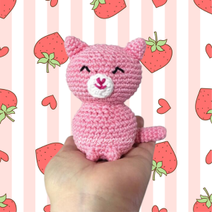 A pink cat with white muzzle being held against a background with pink and white stripes with strawberries and hearts