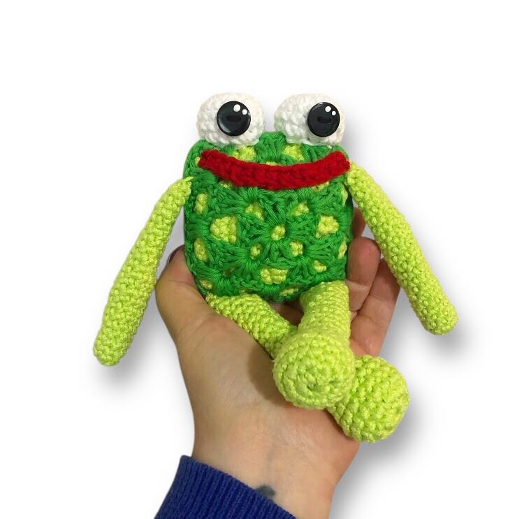 Hand holding a green crochet frog toy against a white background