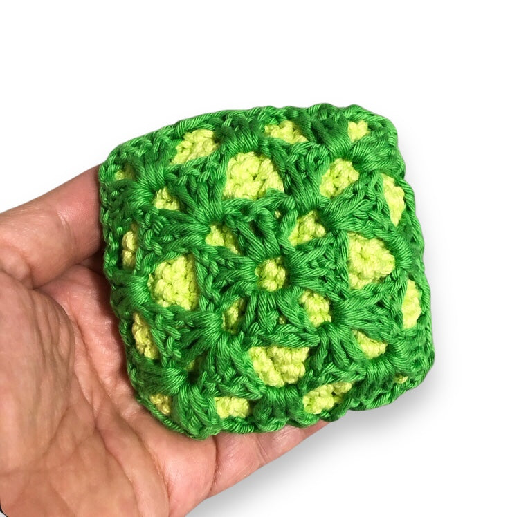 Green and yellow crocheted square held in a hand against a white background