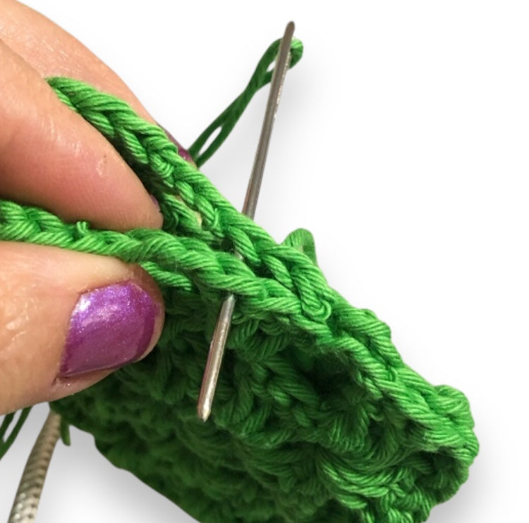 Close-up of green yarn being crocheted with a needle on a white background