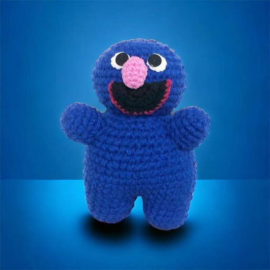 A crocheted version of Grover from Sesame Street standing against a blue background. 